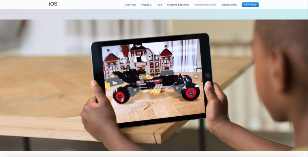 Image shows a child, seated at a table, holding a tablet. The image on the tablet appears to be a robotic car, viewed with AR as sitting on the table the child is at.