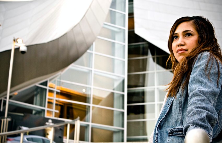 Image of a woman in a denim jacket standing in front of office buildings