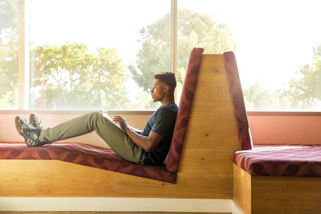 Young man sitting at a booth typing on his laptop.